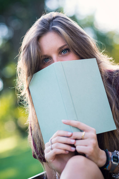 Young woman hiding behind a book in the park.  - Foto, Bild