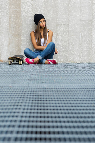Teenager with skateboard portrait sit against concrete wall.  - Fotó, kép