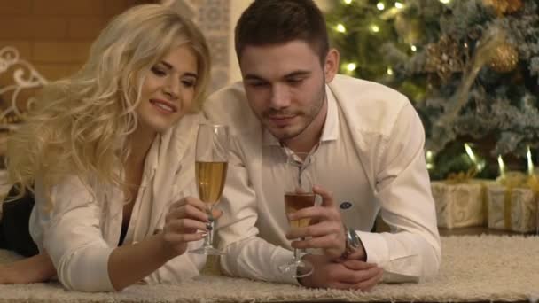 Young Happy Couple Holding Glasses With Champagne At Floor Near Christmas Tree - Materiał filmowy, wideo