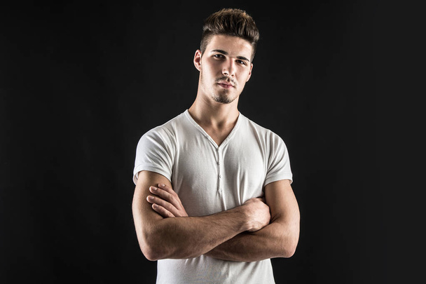 Portrait of confident young man wearing white shirt with crossed arms against black background.  - Foto, Imagem