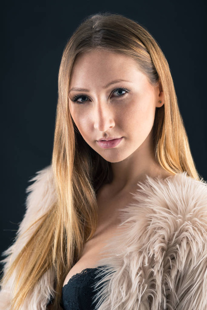 Close up portrait of attractive blond woman with fur against black background. - Photo, image