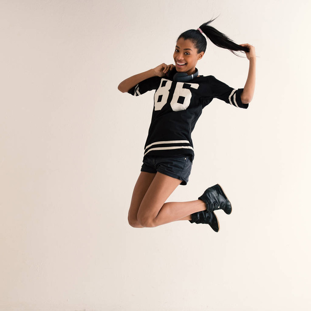 Jumping brazilian girl full body portrait with headphones. Filtered image. - Photo, Image