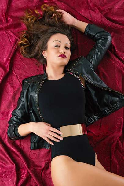 Fashion woman portrait laying down on the floor on dark red fabric background. Studio image. - Zdjęcie, obraz