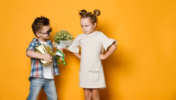little boy gives a bouquet of daisies to his girlfriend a girl. The girl angrily folded her arms in front of her and did not want to take a gift. Concept of friendship, quarrel, date - Zdjęcie, obraz
