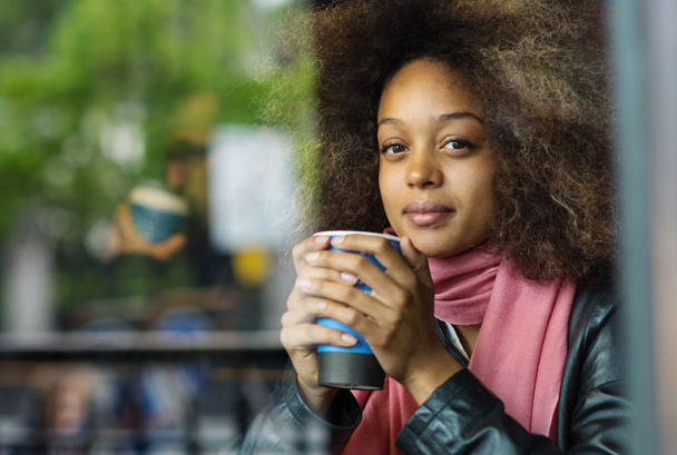 Happy young woman portrait drinking coffee inside a cafe. Image shot through a window. - Фото, зображення
