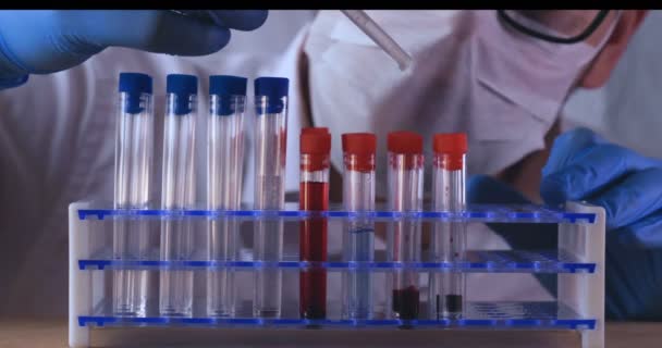 Лабораторних робіт, лікар тримає pipette, в медичній масці і окулярах, приймає тест з випробувальної трубки в синіх рукавичках, аналіз, кров, ДНК, тримач пробіркою. - Кадри, відео
