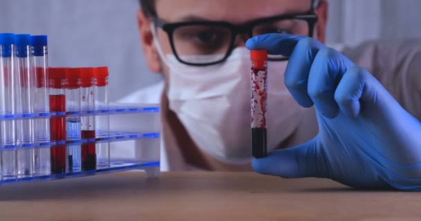 Lab work, the doctor holds a pipette, in a medical mask and glasses, takes a test from a test tube in blue rubber gloves, analysis, blood, DNA, a test tube holder. - Video