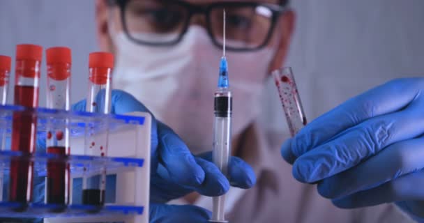 Lab work, the doctor holds a pipette, in a medical mask and glasses, takes a test from a test tube in blue rubber gloves, analysis, blood, DNA, a test tube holder. - Materiał filmowy, wideo