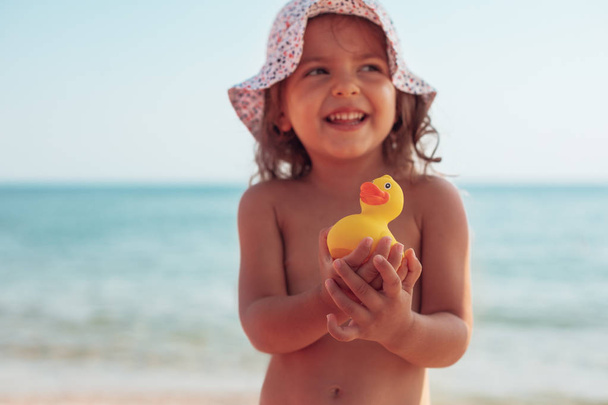 Little girl holding in hands yellow rubber duck toy on the beach - Photo, Image