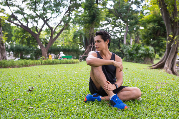 Man relaxing on the ground inside city park. Athlete exercising outdoor in Lumpini Park, Bangkok. - Foto, Imagen