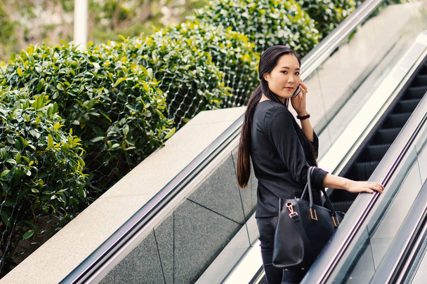 Young businesswoman portrait talking at the phone on escalators. Hong Kong. - Photo, image