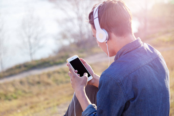 teen boy listens to music in headphones in the phone, black isolated screen of the phone - Photo, Image