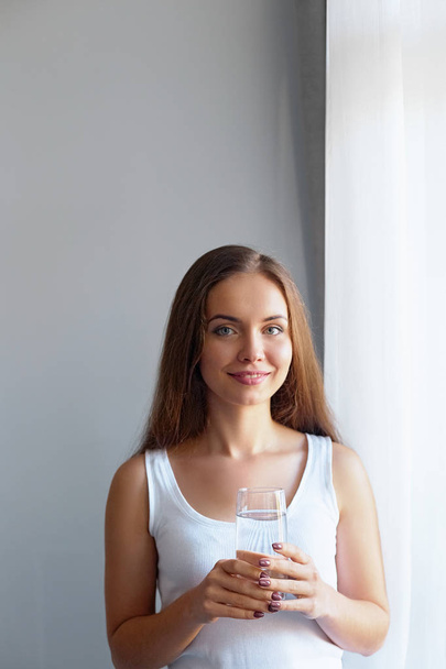 Healthy lifestyle.Young woman drinking from a glass of fresh water. Healthcare. Drinks. Portrait of happy smiling female model holding transparent glass. Health,Beauty,Diet concept. Healthy eating - Photo, image