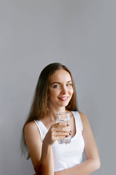 Healthy lifestyle. Portrait of happy smiling young woman posing on isolated studio background, hold water glass. Beautiful girl portrait. Female model poses.  - 写真・画像