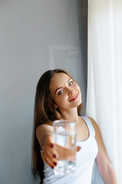 Closeup young woman show glass of water. Portrait of happy smiling female model holding transparent glass of water.Healthy lifestyle. Beauty, Diet concept  - Photo, image