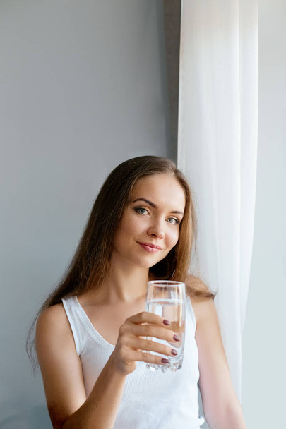 Healthy lifestyle.Young woman drinking from a glass of fresh water. Healthcare. Drinks. Portrait of happy smiling female model holding transparent glass. Health,Beauty,Diet concept. Healthy eating - Valokuva, kuva