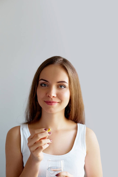 Healthy Diet Nutrition. Portrait Of Beautiful Smiling Young Woman Taking Vitamin Pill. Closeup Of Happy Girl Holding Colorful Capsule Pill And Glass Of Fresh Water. Dietary Supplement - Foto, afbeelding