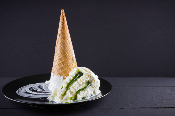 Ice cream cone on black background, summer concept. Dessert with jam on black plate. Waffle cone with ice cream in minimalism style. Copy space - 写真・画像