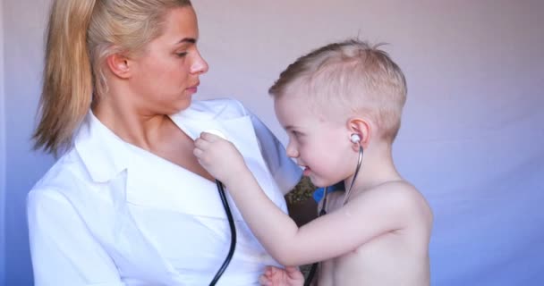 若い看護婦は聴診器を使用して子供の肺に耳を傾け、次に患者の耳および温度を点検し、マスクを取除き、前装置、病院で、ポリクリン (家で) 医者を、すぐに点検する. - 映像、動画