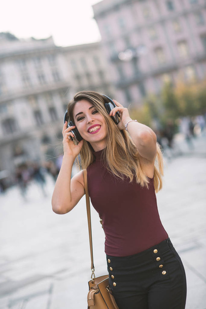 Happy young beautiful blond woman relaxing listening to music with earphones in the city. Milan, Italy. Lifestyle concept of youth, fun, enjoy life. - Zdjęcie, obraz