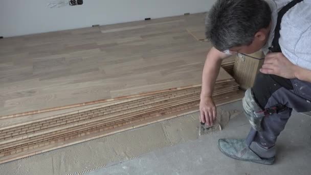 Hombre con espátula aplicar adhesivo de madera en el suelo de hormigón
 - Imágenes, Vídeo