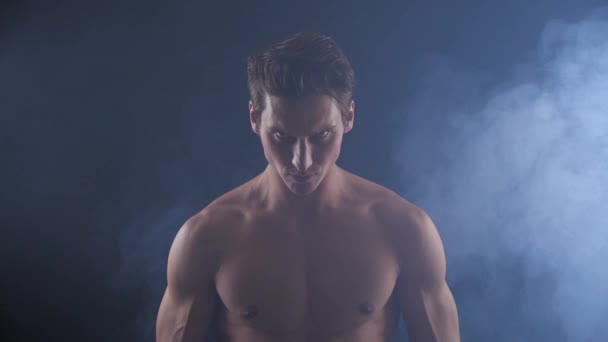 Handsome shirtless man standing on dark background, with smoke around him. - Footage, Video