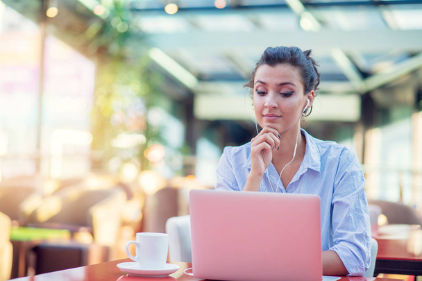 Image d'une femme heureuse utilisant un ordinateur portable alors qu'elle était assise au café. Jeune femme assise dans un café et travaillant sur un ordinateur portable
. - Photo, image