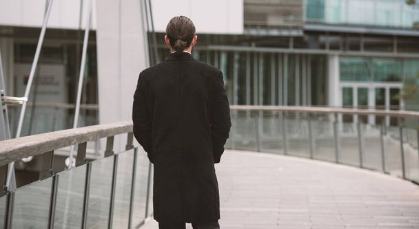 Young businessman portrait walking on futuristic pedestrian bridge at the Defense District. Paris, France. View from behind. - 写真・画像