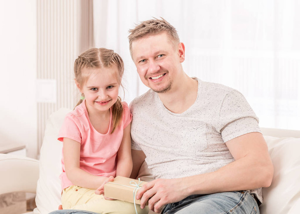 Dad with daughter opening Fathers day gift on sofa - Fotoğraf, Görsel