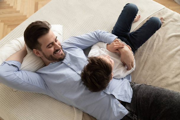 Happy dad lying on bed talking with little son - 写真・画像