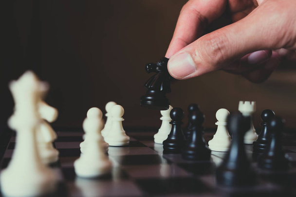 Hand of businessman making move with black knight on chess board - Photo, image