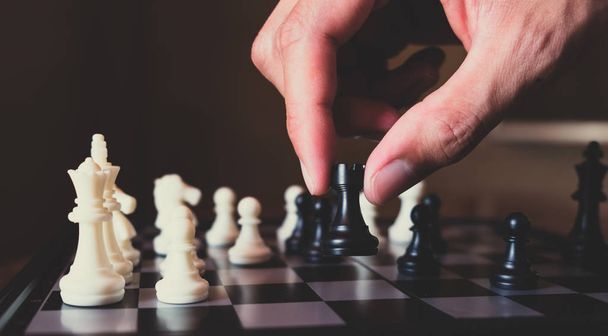 Hand of businessman making move with black rook on chess board - Foto, afbeelding