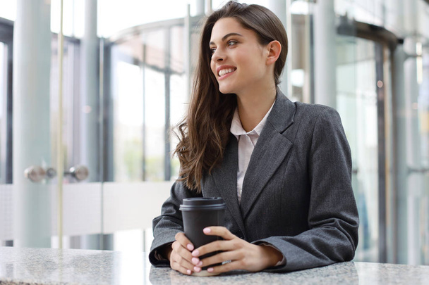 Attractive smiling businesswoman standing in the office with a cup of coffee. - Foto, afbeelding