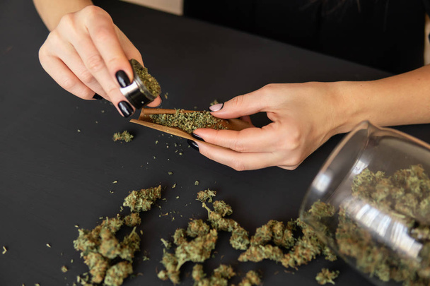 Close up of marijuana blunt with grinder. Woman preparing and rolling marijuana cannabis joint. Marijuana use concept. Woman rolling a marijuana joint. - Photo, Image