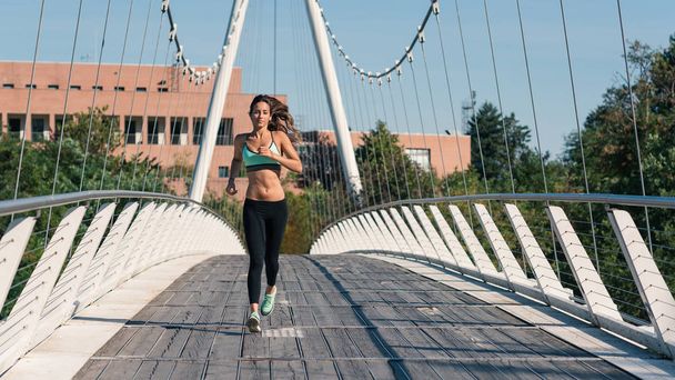 Young woman running outdoors on a modern bridge. Full body portrait. - Foto, imagen
