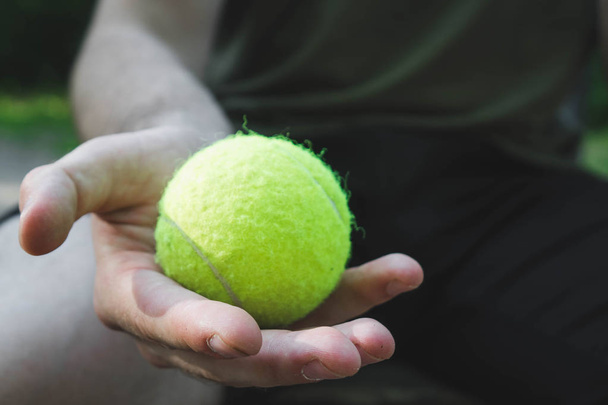 мужчина держит зеленый теннисный мяч на улице
 - Фото, изображение