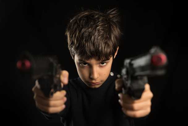 Kid against black background holding guns. Studio portrait. - Foto, Imagen