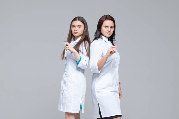 Two female doctors standing back-to-back hold ready-to-inject syringes - Zdjęcie, obraz