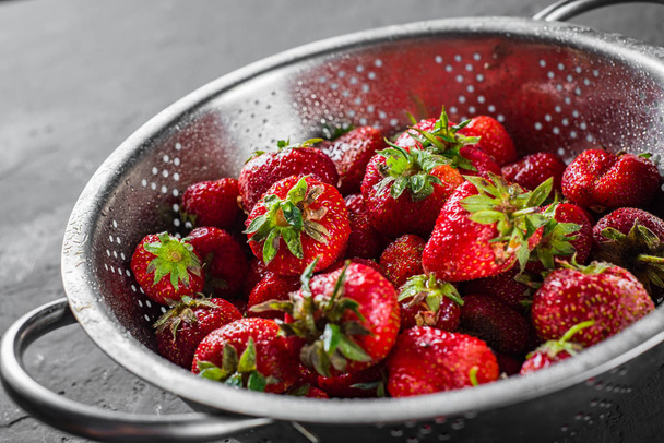 Fresh juicy red strawberries in stainless steel colander on Dark grey black slate background - Фото, зображення