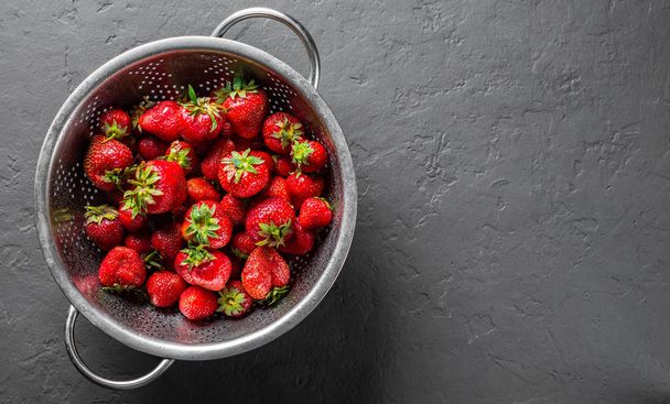 Fresh juicy red strawberries in stainless steel colander on Dark grey black slate background - Фото, зображення