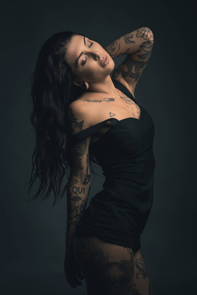Sexy woman studio portrait with black dress and tattoos against  - Фото, зображення