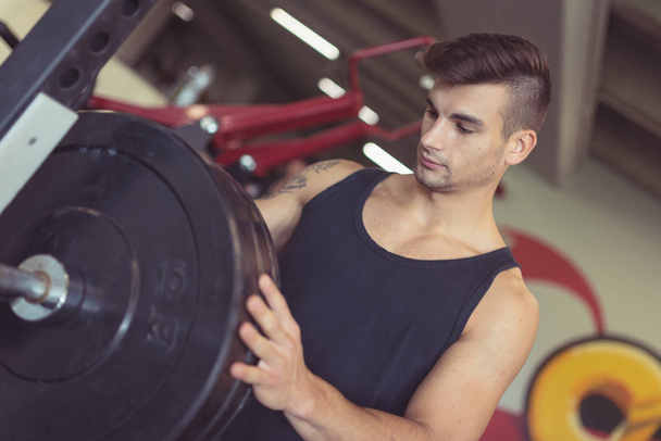 Young sporty man portrait working out in the gym preparing wheights for squats. Concept of active lifestyle. - Foto, Imagem