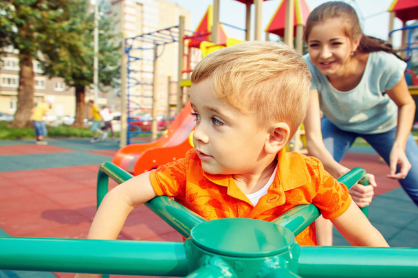 mały chłopiec na placu zabaw. grając dziecko z matką na Wesoła go round - Zdjęcie, obraz