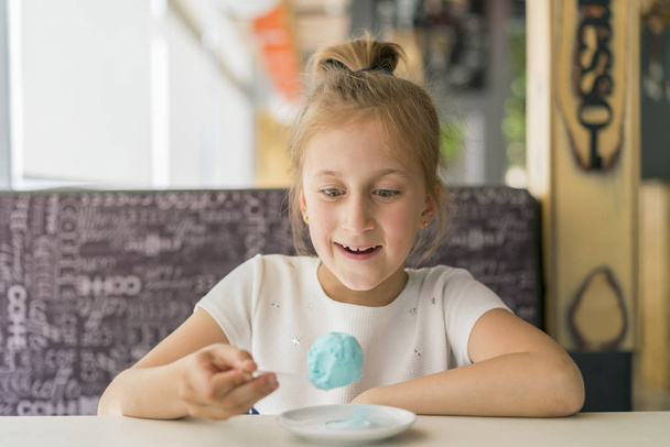 Little girl eating blue ice cream in a cafe. Girl delighted with ice cream. Adorable little girl eating ice cream at summer - Foto, afbeelding