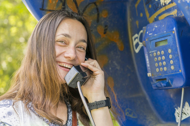Όμορφη νεαρή γυναίκα σε τηλεφωνικό θάλαμο. Το κορίτσι μιλάει στο τηλέφωνο από το καρτοτηλέφωνο. όμορφη γυναίκα που μιλάει με το δημόσιο τηλέφωνο - Φωτογραφία, εικόνα