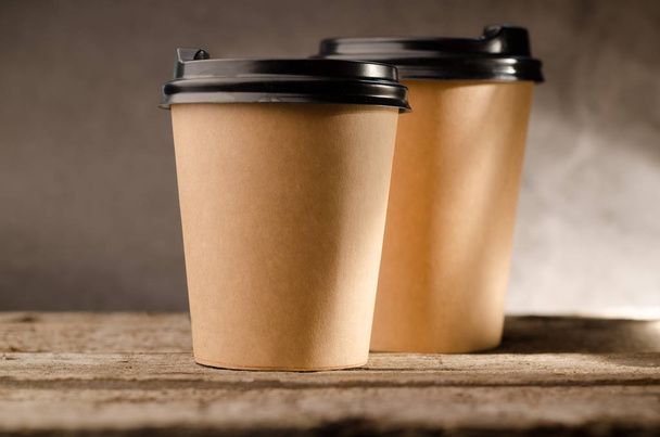 Paper mug with coffee to go against wood background. - Фото, зображення