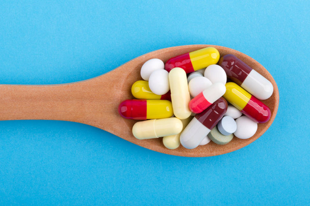 Comprimidos de medicina e cápsulas em colher de madeira
 - Foto, Imagem