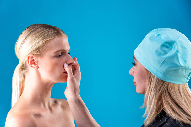 Kosmetikerin zieht Korrekturlinien im Gesicht der Frau. vor der plastischen Operation. isoliert auf blau - Foto, Bild
