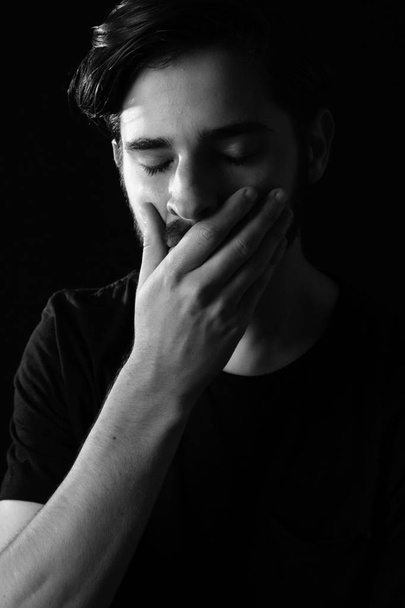 Close up of young adult male eyes closed hand over mouth in shock or horror. Monotone, black and white for dramatic effect, dark and moody series. Concept image for distress or realization of actions. - Fotoğraf, Görsel