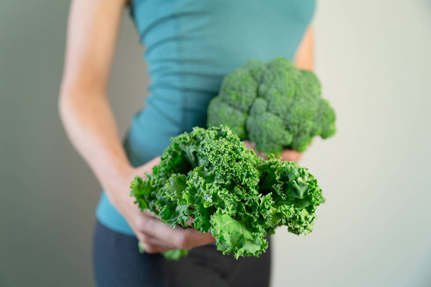 Woman in sport wear holding broccoli and kale. Healthy lifestyle - Foto, imagen